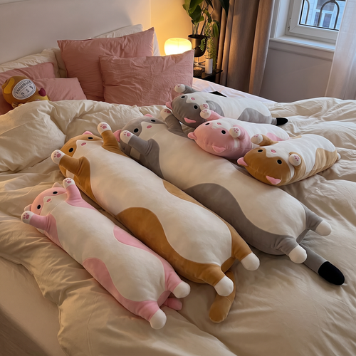 Snug Cat long plushies in every size and colour stacked on a bed